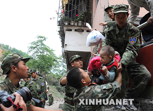 5月13日，在震后的北川縣城，武警戰(zhàn)士將一名和家人失散的幼童救出。 記者從四川省綿陽市抗震救災(zāi)指揮部了解到，受災(zāi)特別嚴重的北川縣老縣城80%、新縣城60%以上的建筑物因地震垮塌，縣城周邊發(fā)生大面積山體滑坡。