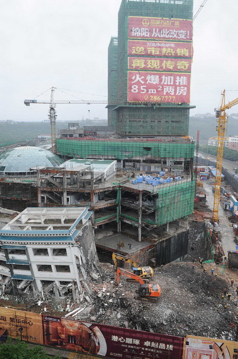 5月21日，工程機械在拆除綿陽紫荊民族中學校舍，旁邊則是建設(shè)中的萬達廣場。