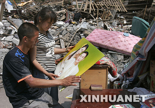 5月19日，雖然相框損壞了，夫妻倆還是仔細(xì)地把結(jié)婚照擦拭干凈。 四川省什邡市鎣華鎮(zhèn)仁和村三組的梁正彬一家很幸運(yùn)，大地震發(fā)生時，包括老父母和年幼女兒在內(nèi)的全家5口人都跑出了轟然倒塌的房屋?！捌桨簿褪歉＃　彼麄兡帐皬U墟中的家，準(zhǔn)備重建家園。